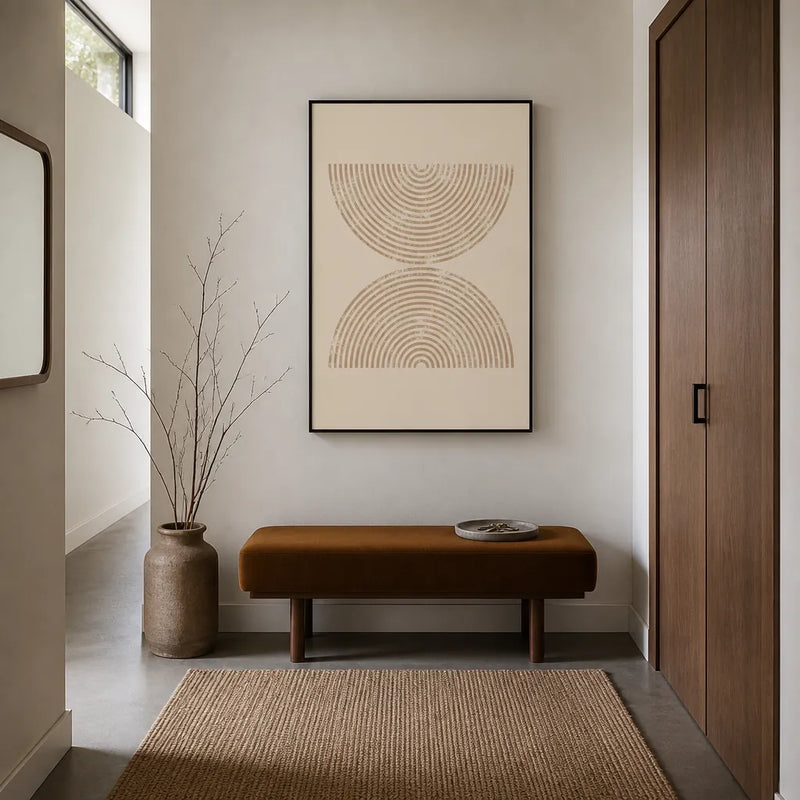 Mid-century modern art print of warm beige nested arches on cream, framed on a white wall above a rust-brown velvet bench with a jute rug and walnut door in a sunlit hallway
