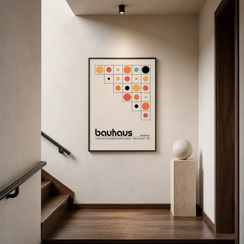 Bauhaus exhibition-style art print, a grid of primary-coloured dots with lowercase 'bauhaus' type, framed on a stairwell wall beside a travertine plinth